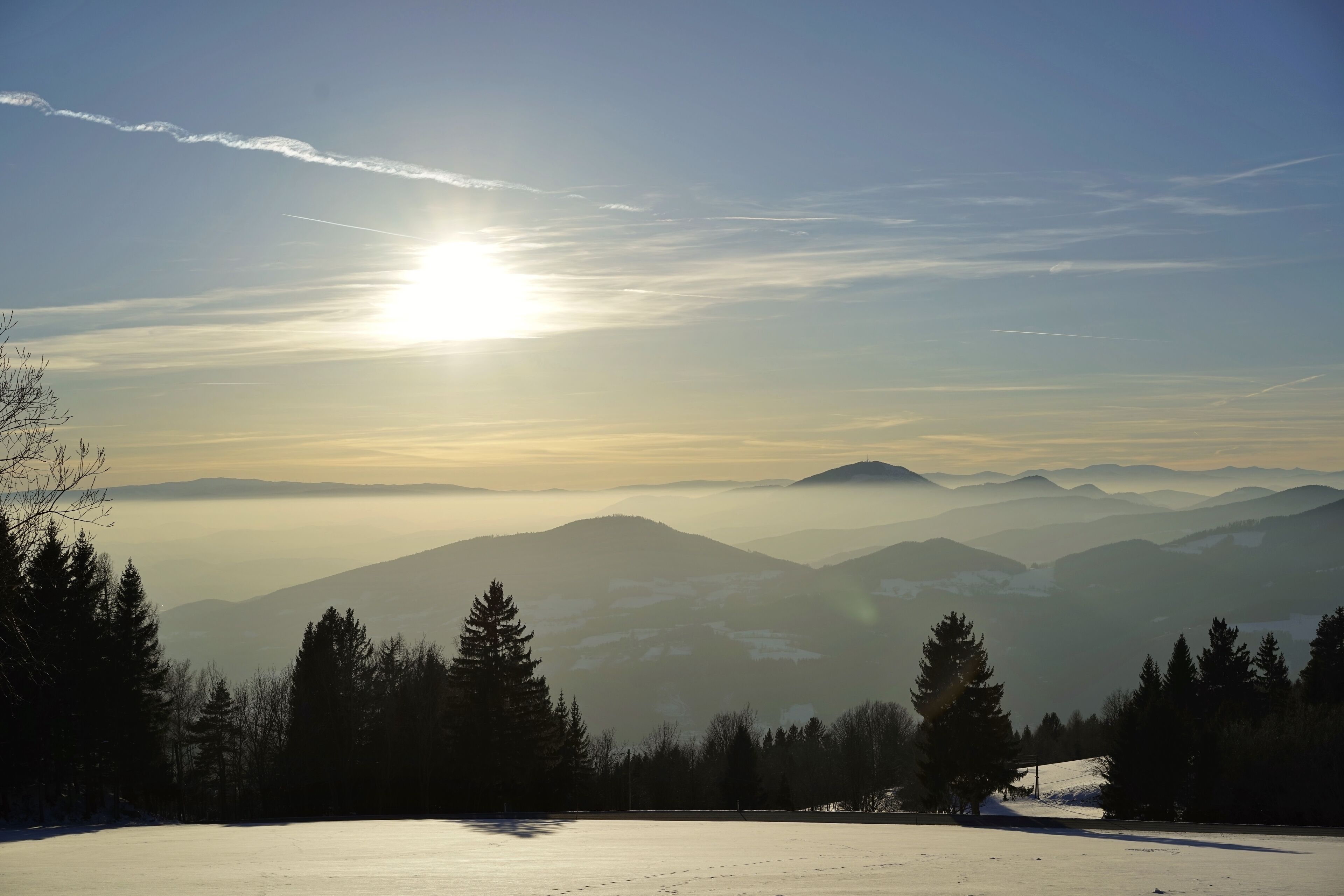 Eine verschneite Landschaft mit Bergen und Bäumen unter blauem Himmel.