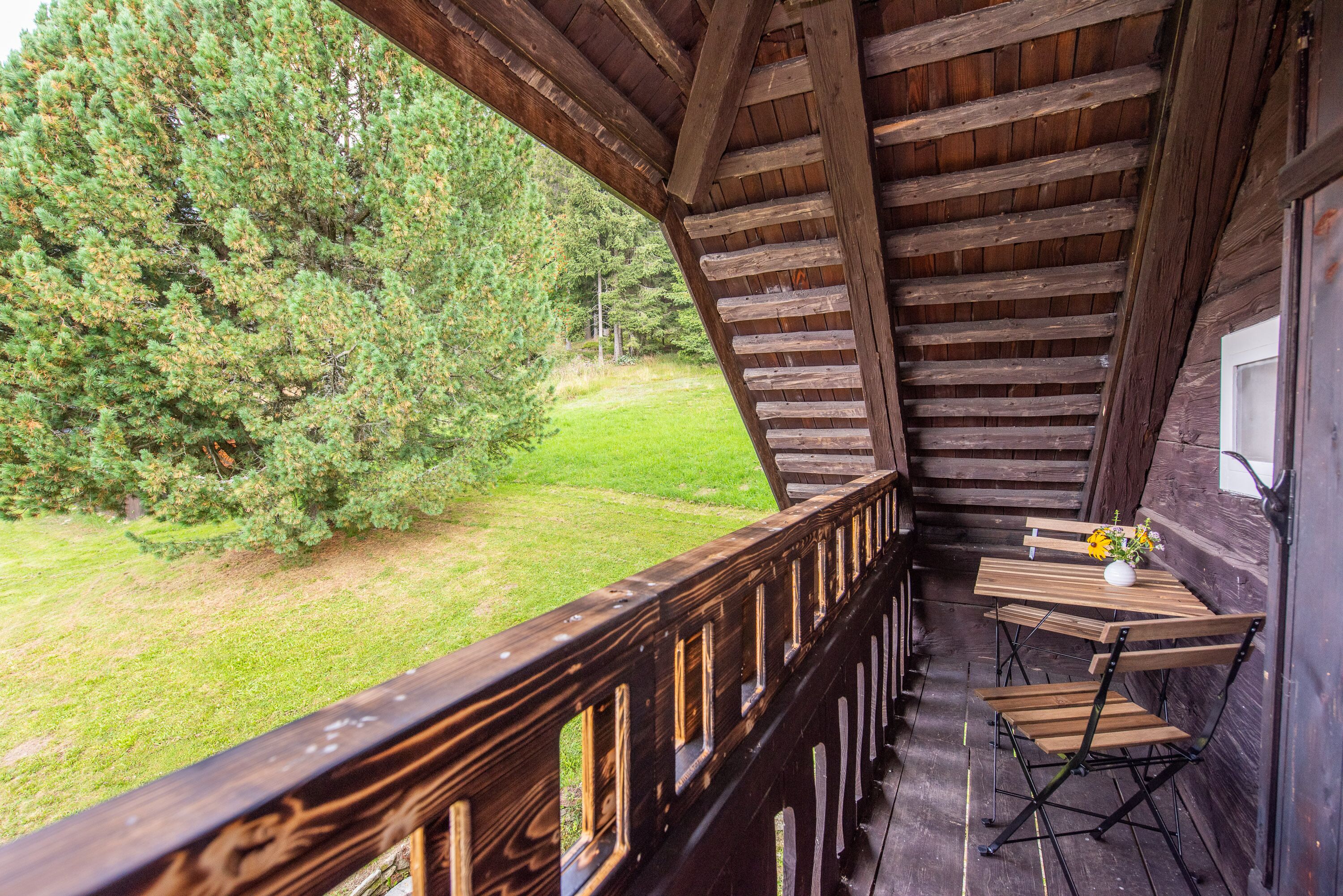 Ein Holzbalkon mit Tisch und Stühlen, der auf eine Wiese und Bäume blickt.