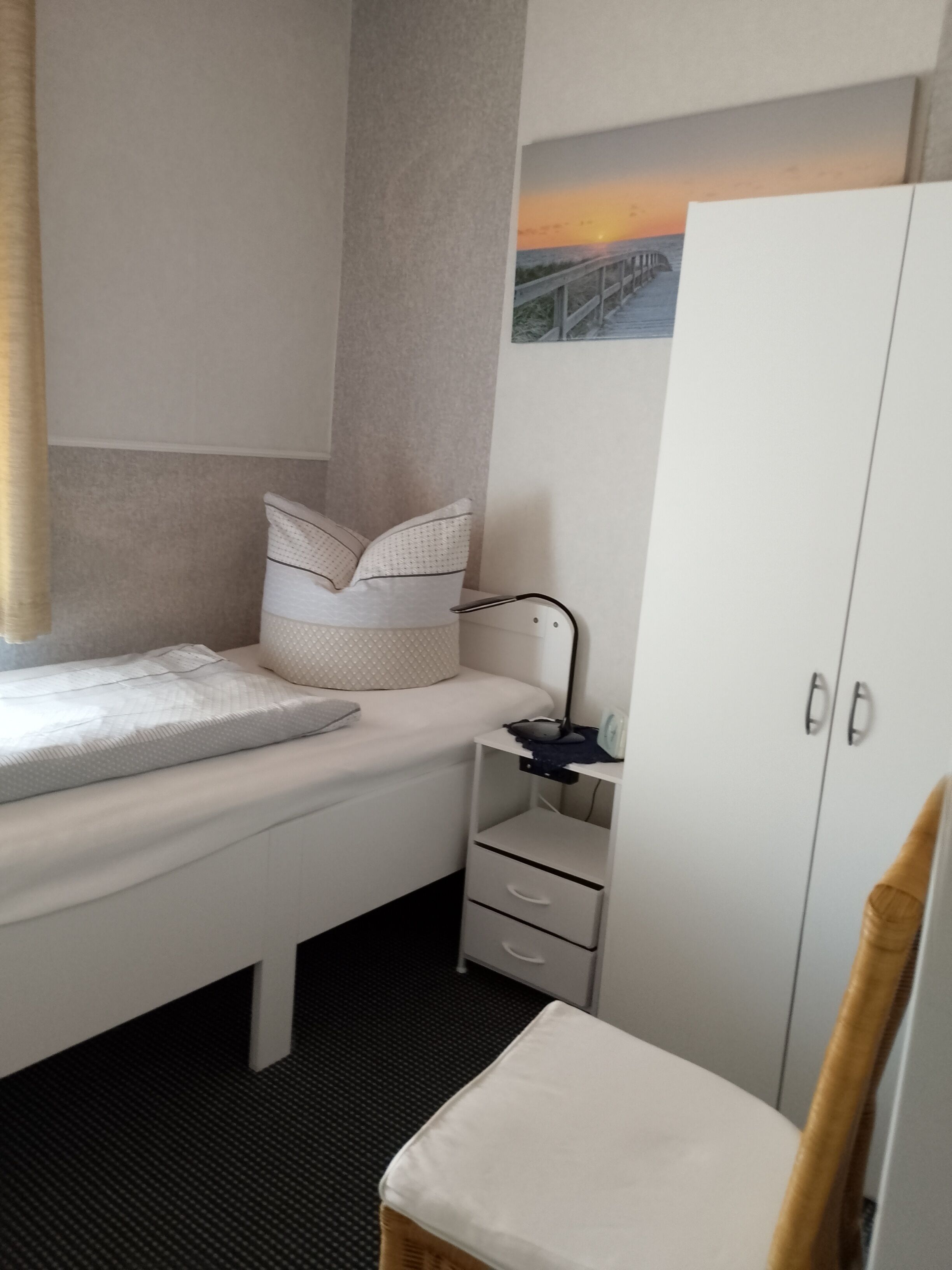 A compact bedroom with a bed, a small desk, a wardrobe, and a painting on the wall.