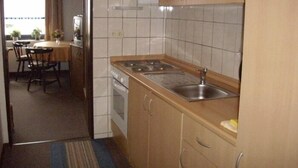 A compact kitchen with a stove, sink, and cabinets. There is a dining area with a table and chairs visible through an open doorway. - Small and cozy holiday home. Quiet Location (Bunde)