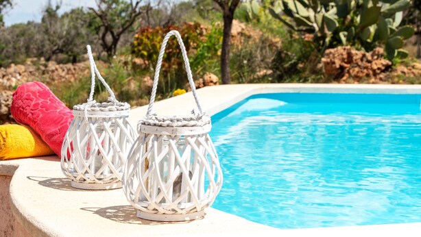 Deux lanternes blanches, suspendues à des cordes, sont posées sur le bord d’une piscine, avec la piscine elle-même en arrière-plan.