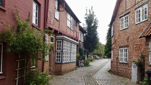 A cobblestone street flanked by red brick buildings with white-framed windows. - LÜNEBURG: Idyllic, bright garden house in the center of a historic half-timbered town (Lüneburg)