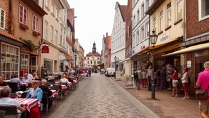 A cobblestone street lined with buildings, outdoor seating for cafes, and pedestrians. - LÜNEBURG: Idyllic, bright garden house in the center of a historic half-timbered town (Lüneburg)