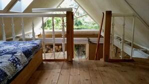 A room with a sloped ceiling, wooden flooring, a bed with a patterned blanket, a desk with a chair, and a window with a view of greenery. - LÜNEBURG: Idyllic, bright garden house in the center of a historic half-timbered town (Lüneburg)