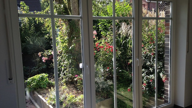 A sliding glass door leading to a garden with various plants and flowers. - Holiday house in the idyllic holiday resort at the lighthouse (Krummhörn)