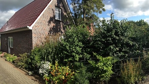 A brick house with a red roof, surrounded by lush greenery and a metal fence. - Holiday house in the idyllic holiday resort at the lighthouse (Krummhörn)