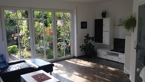 A living room with a sofa, a coffee table, a TV, and a sliding glass door leading to a garden. - Holiday house in the idyllic holiday resort at the lighthouse (Krummhörn)