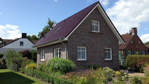 A two-story house with a brick facade, a steeply pitched roof, and a small front porch. - Holiday house in the idyllic holiday resort at the lighthouse (Krummhörn)