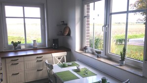 A kitchen with a dining table set for two, a coffee maker, and potted plants on the windowsill. - Holiday house in the idyllic holiday resort at the lighthouse (Krummhörn)