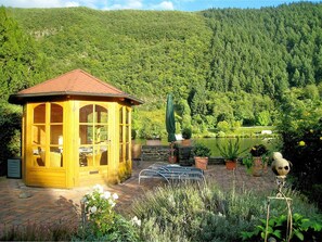 Un porxo de fusta amb teulada, envoltat d'un jardí ple de plantes en testos i una bassa.