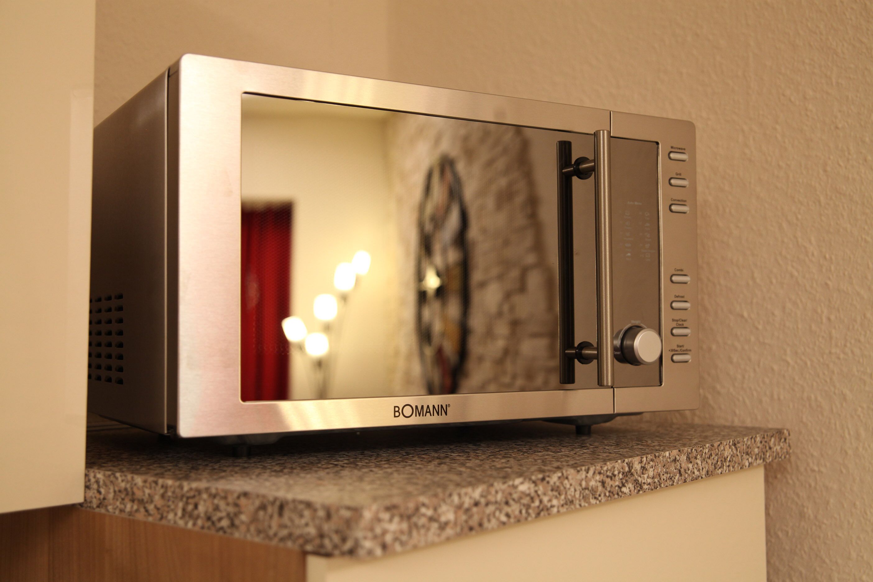 A stainless steel microwave oven with a digital display, placed on a granite countertop.