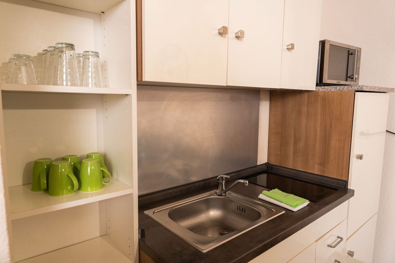 A kitchen with a stainless steel sink, a microwave, and shelves with green mugs.
