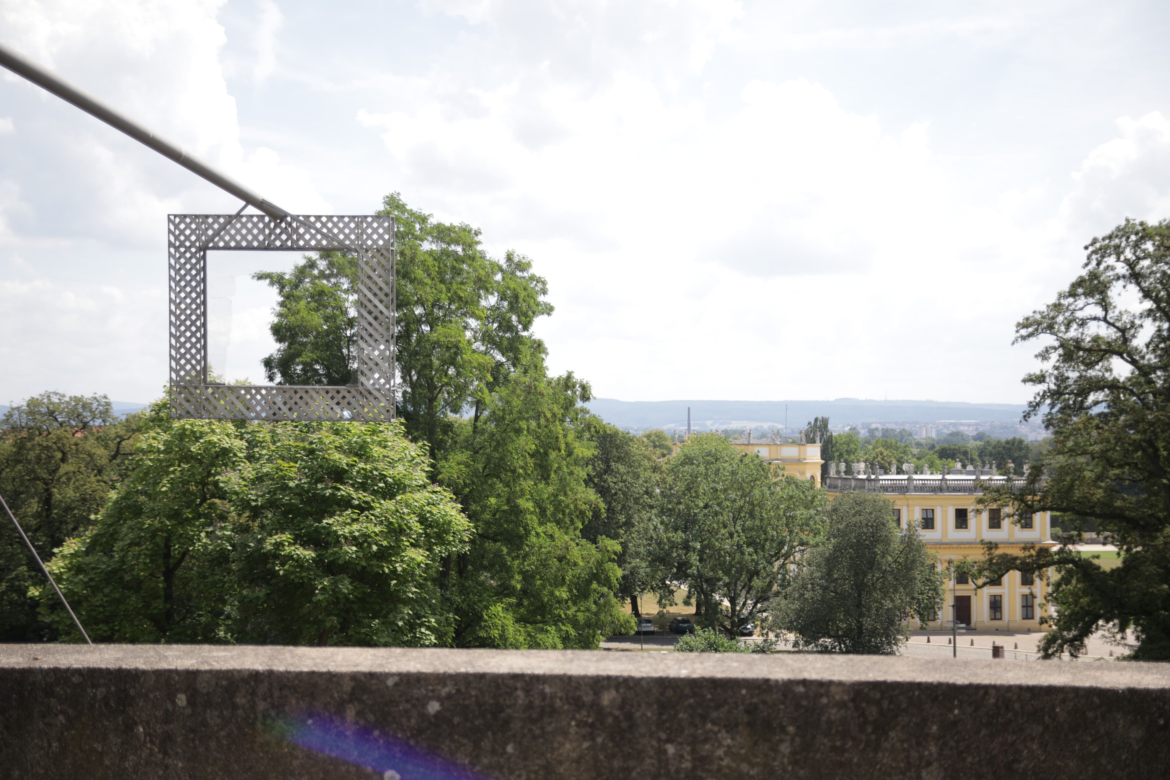 Blick auf eine Stadtlandschaft mit einem markanten Gebäude im Hintergrund, umgeben von üppigem Grün.
