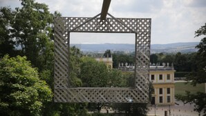 Une structure en treillis métallique offrant une vue sur un bâtiment et des arbres en arrière-plan.