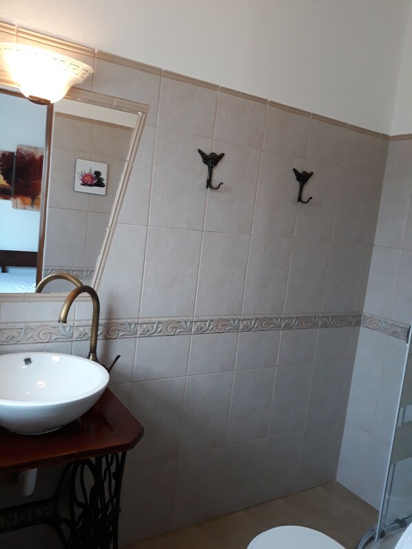 Un baño con lavamanos blanco, grifo de latón y espejo. Hay dos ganchos en la pared y un borde de azulejos decorativo.