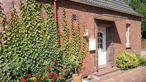 Ein Backsteinhaus mit weißer Tür, einer kleinen Veranda und einem Backsteinweg, der zum Eingang führt.