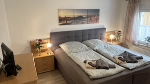 Ein Schlafzimmer mit einem großen Bett, Nachttischen, einem Schreibtisch und einem Fenster mit Vorhängen.