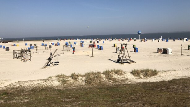 Ein Strand mit vielen blauen und bunten Strandhütten, einem klaren Himmel und einem weiten Blick auf das Meer.