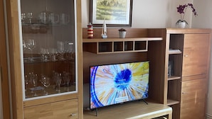 Ein Wohnzimmer mit einer Holzunterhaltungsecke, einer Glasvitrine mit Weingläsern, einem gerahmten Bild und einem Blumentopf.