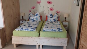 Ein Schlafzimmer mit zwei hölzernen Betten, grüner Bettwäsche, Blumenbildern an der Wand, Nachttischen mit Lampen und einem Holzschrank.