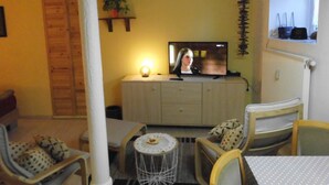 Ein Wohnzimmer mit Fernseher, Esstisch, Stühlen, einem kleinen runden Tisch und einer Topfpflanze.
