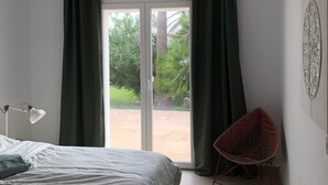 A bedroom with a bed, a chair, a lamp, and a view of greenery outside. - House by the sea, private pool, sea view, roof terrace, air conditioning, WLAN, sep. Studio (Cala Serena)