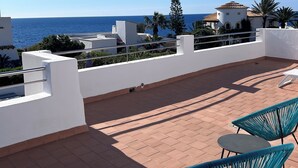 A rooftop terrace with a view of the sea, featuring a white building, palm trees, and two blue chairs. - House by the sea, private pool, sea view, roof terrace, air conditioning, WLAN, sep. Studio (Cala Serena)