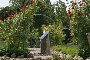 A garden with a stone structure, possibly a fountain, surrounded by lush greenery and flowering plants. - High-quality-modern, approx 65sqm, gr. Garden, exclusive equipment, wirkl. gr. bathroom (Lüneburg)