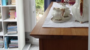 A room with a wooden table, white teapot, and teacups on a white tablecloth. A white bookshelf with books is to the left. - High-quality-modern, approx 65sqm, gr. Garden, exclusive equipment, wirkl. gr. bathroom (Lüneburg)