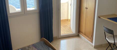 Une chambre à coucher comprenant un lit, un bureau, une chaise, une armoire et offrant une vue sur la mer par les fenêtres.