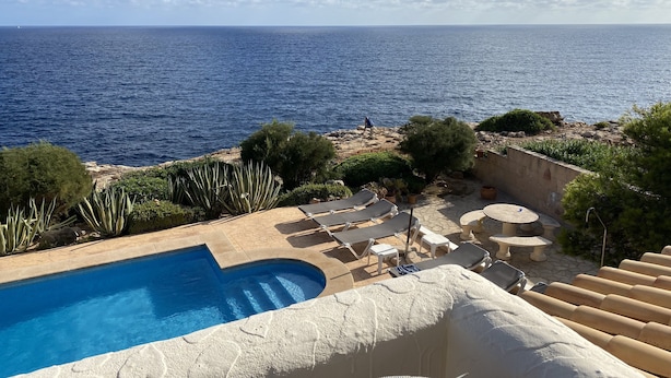 Un espace piscine offrant une vue sur la mer, entouré de verdure et doté de coins salon extérieurs.