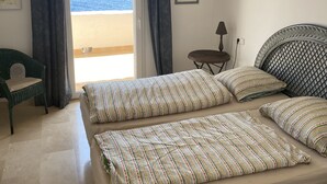Une chambre à coucher avec un lit, une chaise, une petite table et une vue sur la mer.