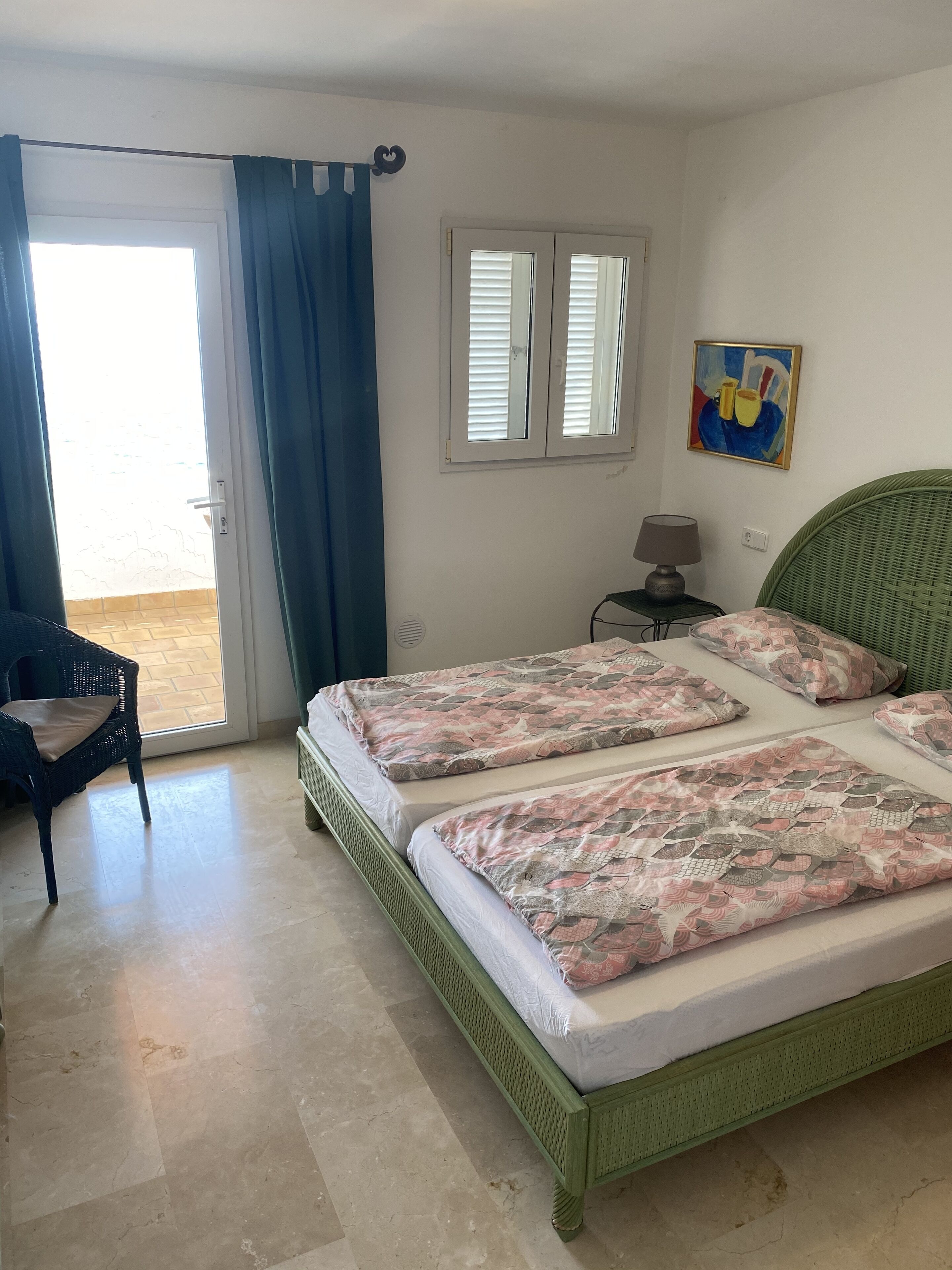 A room with two beds, a chair, a table with a lamp, and a painting on the wall.