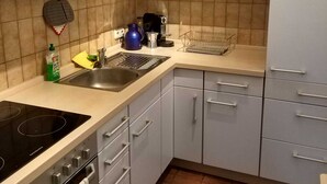 A modern kitchen with white cabinets, a black stove, a sink, and a coffee maker. - 2 room cozy Apartment - Sunny ground floor apartment with garden terrace in Forchheim (Forchheim)