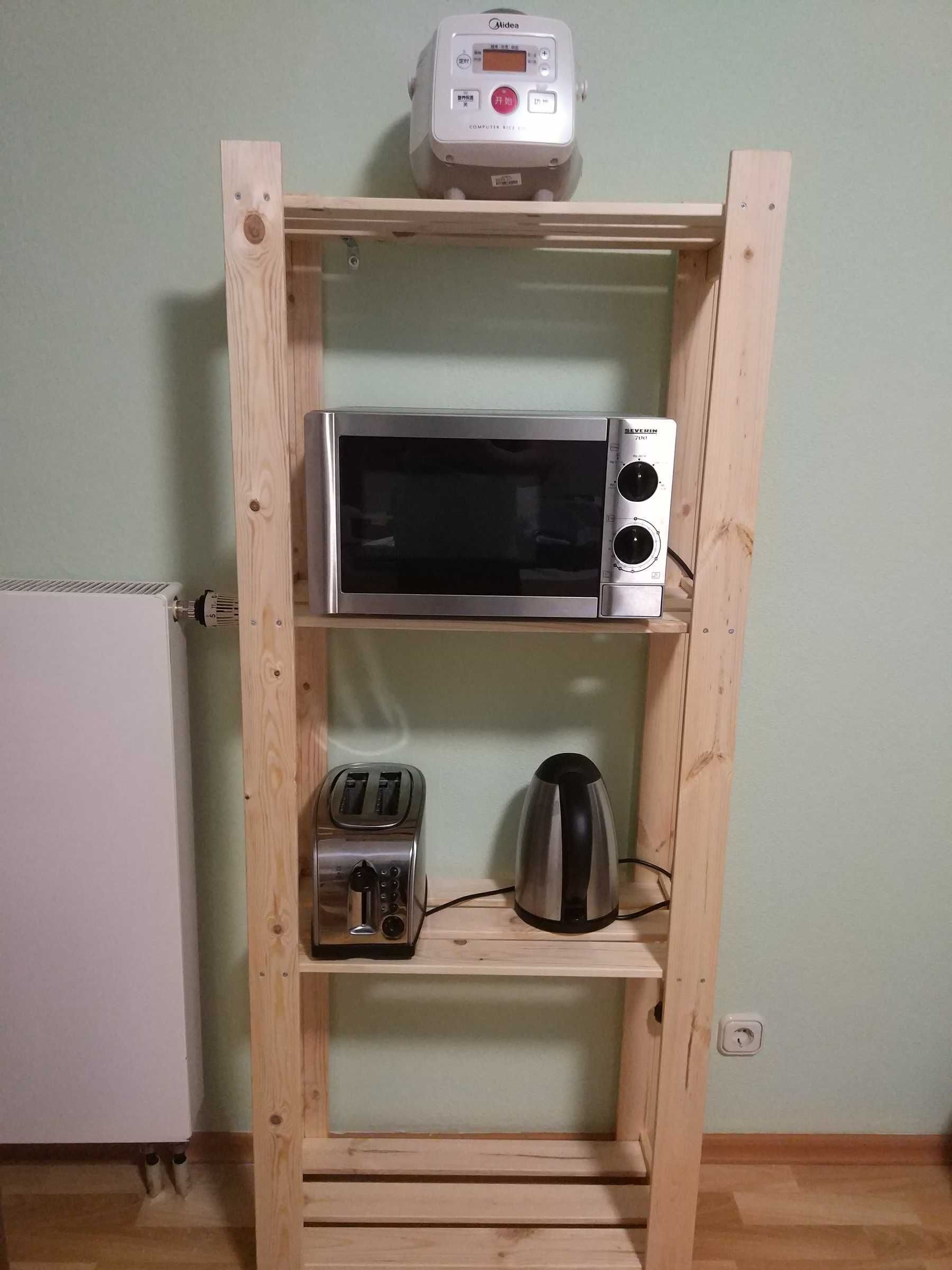 A compact kitchen with a microwave, toaster, and kettle on a wooden shelf unit.