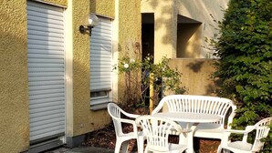 A patio with a round table and four white plastic chairs, a white door, and a small garden area with a tree and a bush. - 2 room cozy Apartment - Sunny ground floor apartment with garden terrace in Forchheim (Forchheim)