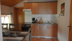 Una cocina compacta con armarios de madera, horno empotrado, lavavajillas y una ventana con cortinas.