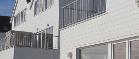 Een wit gebouw met twee verdiepingen, een balkon, een garage en een houten terras met bankjes.