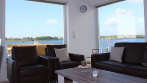 Una habitación con dos sofás de cuero, una mesa de centro de madera y un ventanal con vistas a una masa de agua.