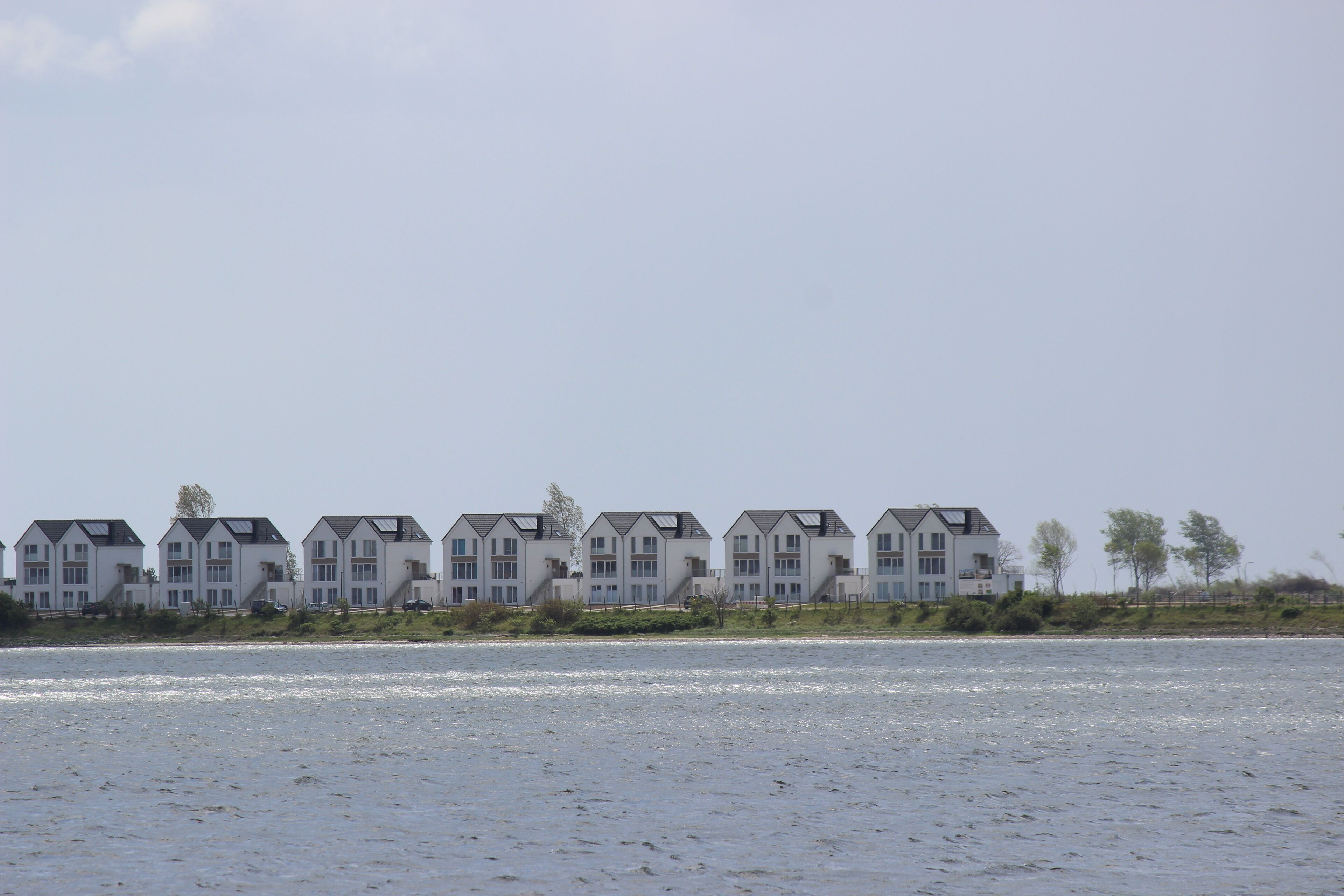 A row of modern, multi-story buildings with a flat roof design, situated along a waterfront.