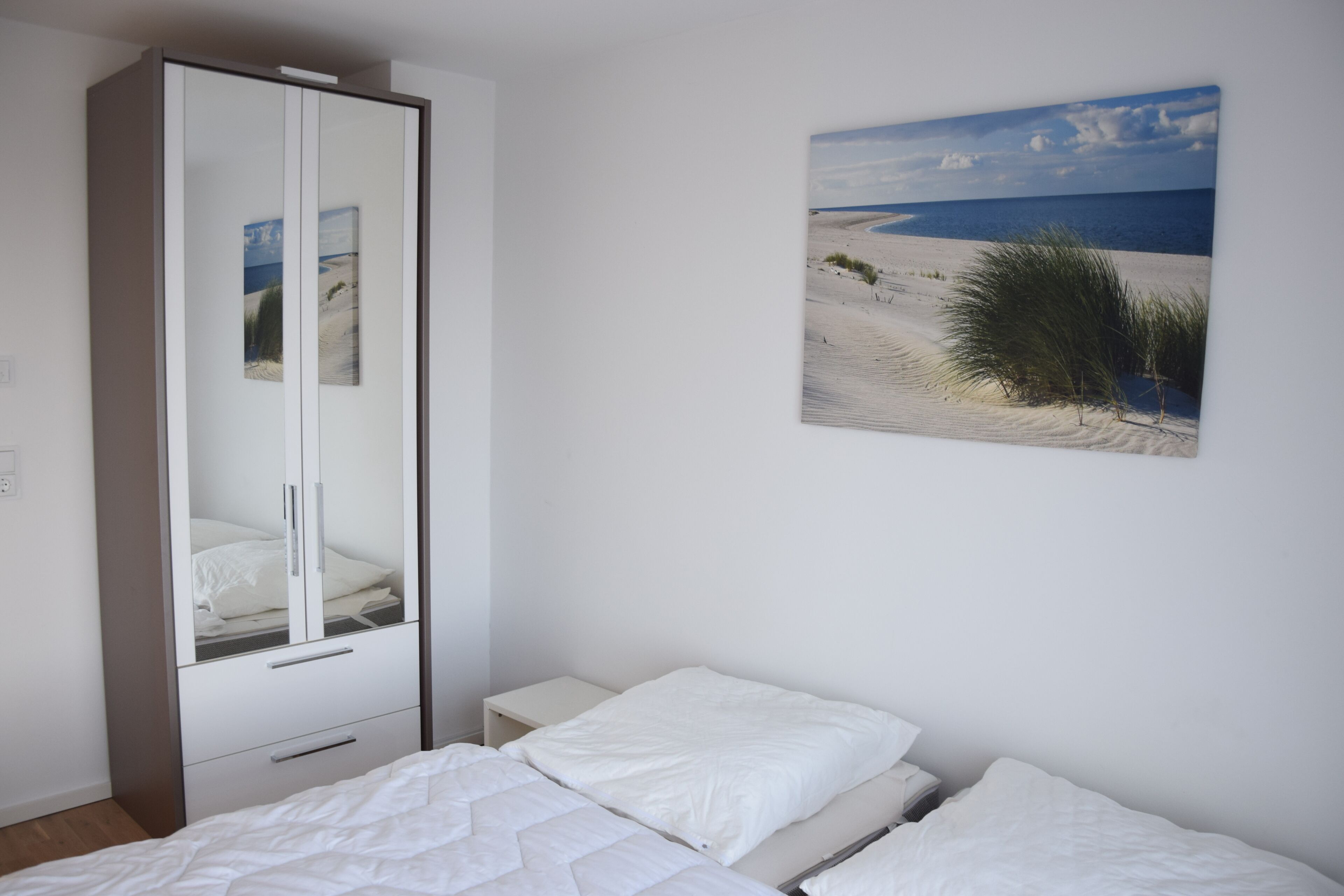 A bedroom with a bed, a wardrobe, and a beach-themed wall art.