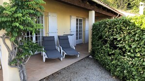 A covered outdoor seating area with two lounge chairs and a table, surrounded by greenery and a gravel path. -  Holiday villa with communal pool, large terrace and magnificent sea views (Gattières)