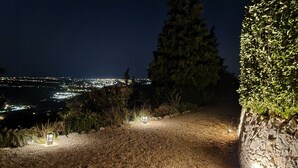 A gravel path with stone walls and a view of a city at night. -  Holiday villa with communal pool, large terrace and magnificent sea views (Gattières)