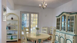 A dining area with a round table, white chairs, a chandelier, and a cabinet with glass doors. -  Holiday villa with communal pool, large terrace and magnificent sea views (Gattières)
