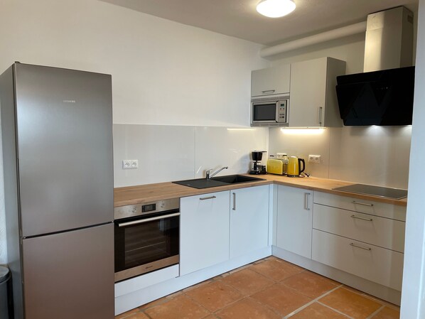 A modern kitchen with white cabinets, a stainless steel refrigerator, an oven, a microwave, and a coffee maker.