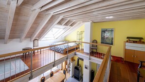 A multi-level interior with wooden beams, a loft bedroom, a dining area, and a kitchen.