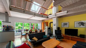 A spacious living area with a high ceiling, a dining area with a table and chairs, a sofa, a TV, and a fireplace.