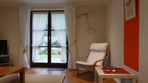 Un salon avec un fauteuil en bois, une petite table, un canapé et un téléviseur.