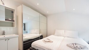 A modern bedroom with a large mirror, a bed with white linens, and a built-in wardrobe.