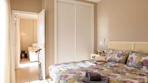 A bedroom with a bed, bedside table, lamp, and a door leading to another room.